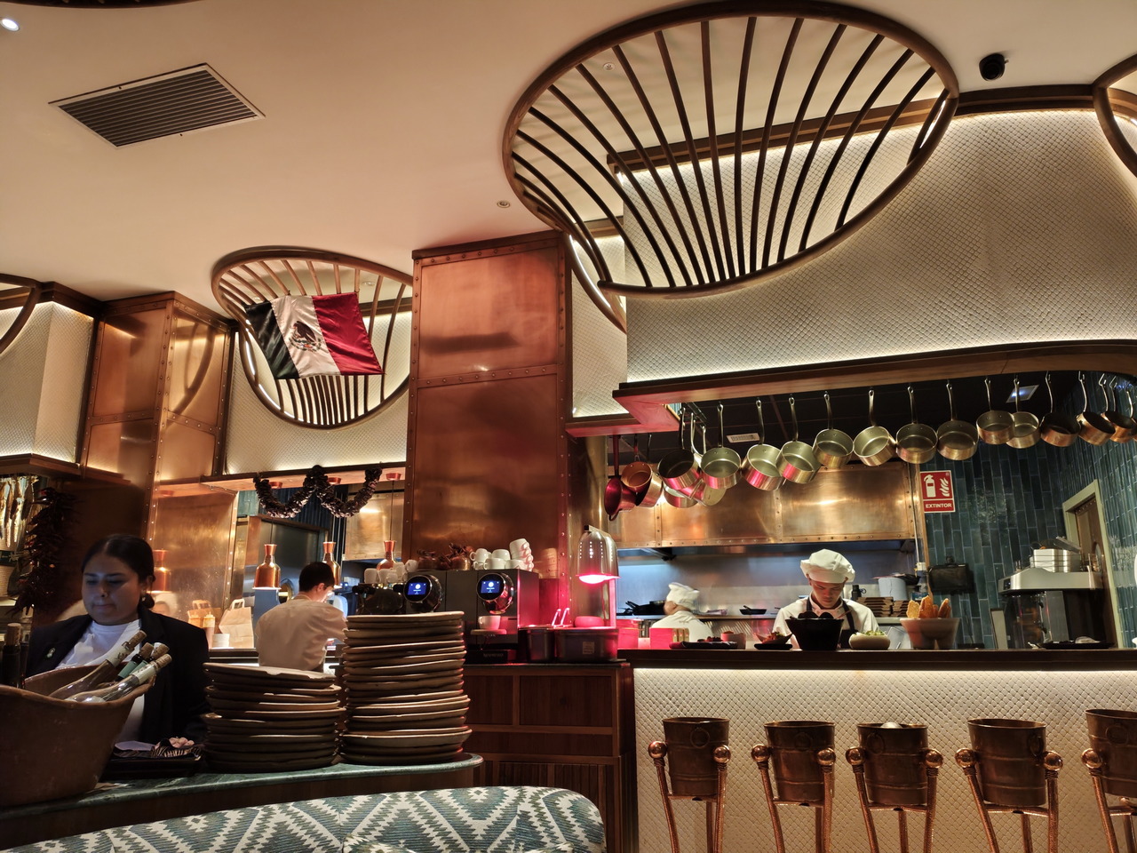 Restaurante mexicano con cocina abierta y decoración moderna, bandera de México y personal trabajando.