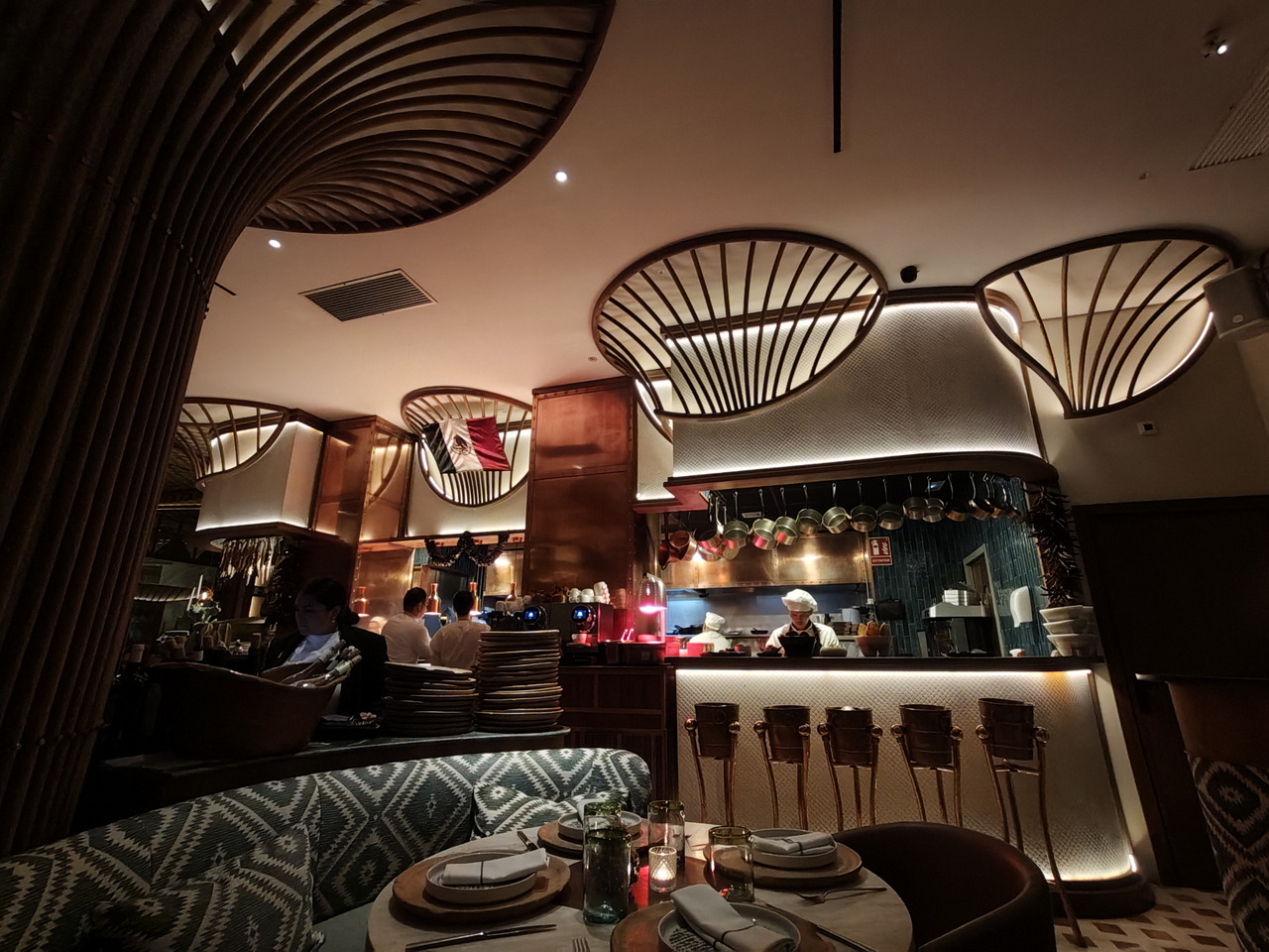 Restaurante elegante con decoración moderna y cocina a la vista, mesas preparadas para clientes.