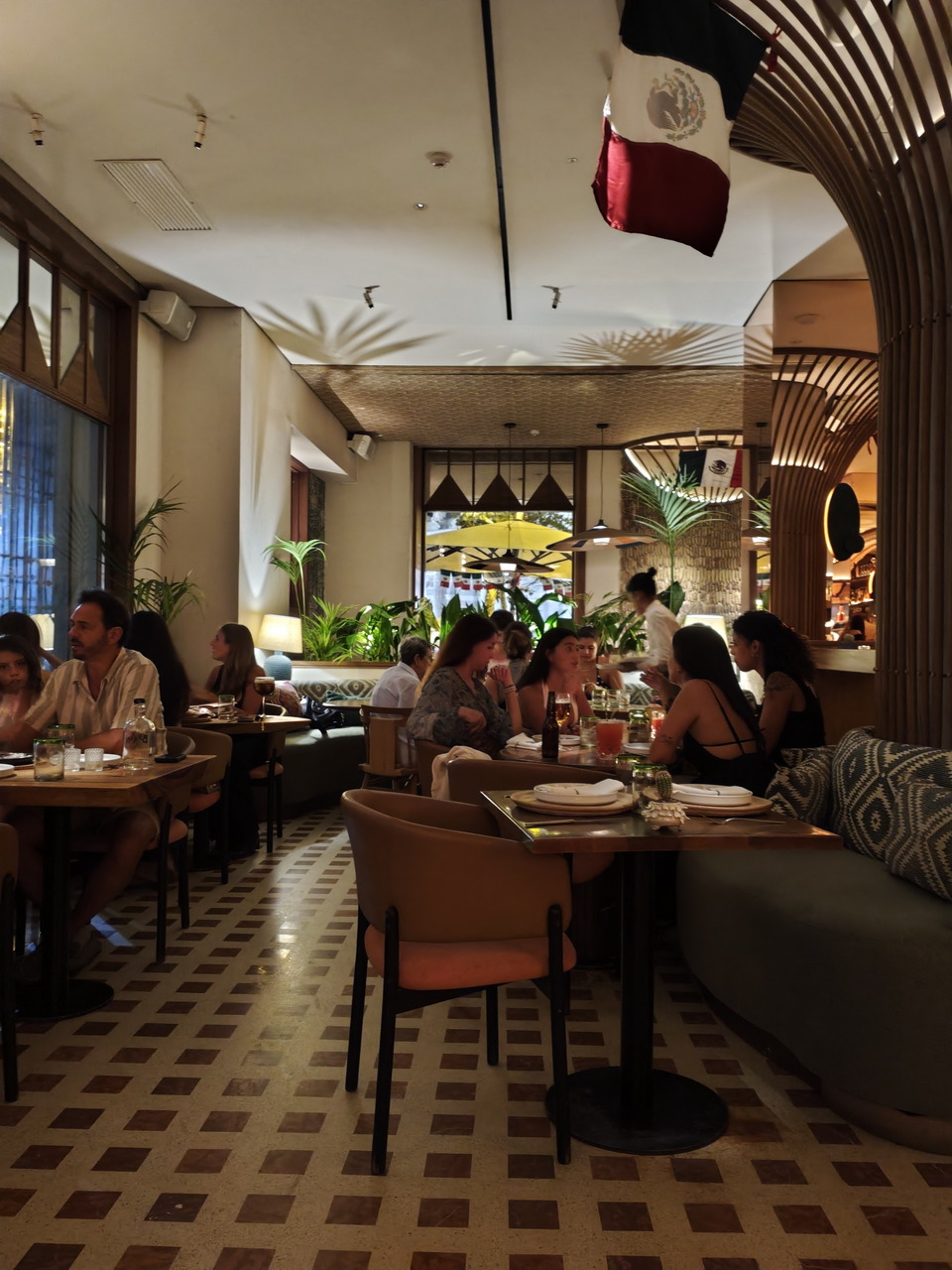 Restaurante mexicano concurrido con ambiente acogedor y bandera nacional izada, mesas llenas de comensales.