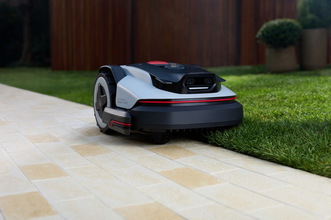 Robot cortacésped automático en jardín, delineando bordes de césped sobre pavimento claro. Tecnología avanzada de jardín.