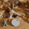 Niño jugando en el suelo con robot aspiradora y juguetes, rodeado de comida y bloques de colores en un salón cálido.