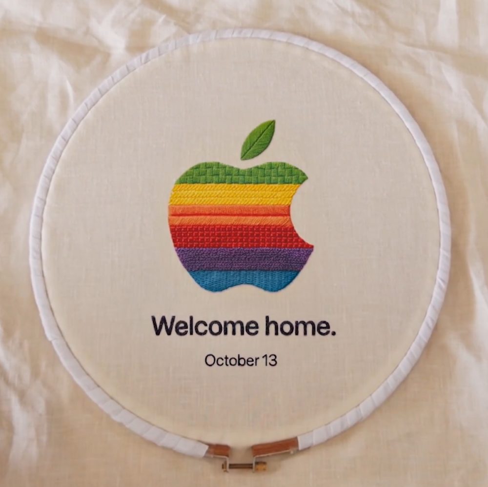 Bordado con logo de manzana multicolor y texto Welcome home y October 13 en un aro de bordar.