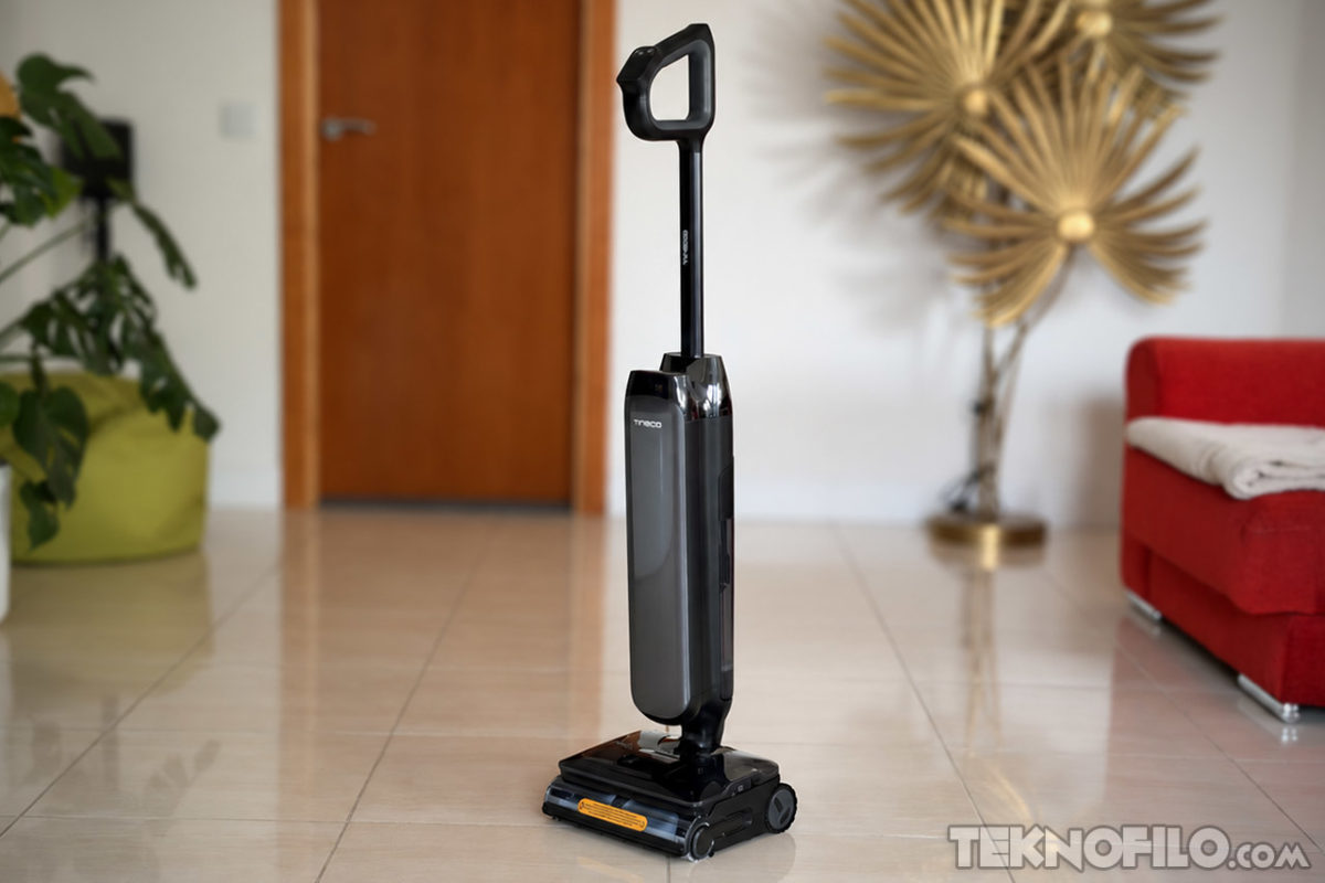 Tineco FLOOR ONE S9 Artist Steam Pro: análisis de sus funciones y opinión Aspiradora vertical negra en salón moderno con suelo de baldosas, sofá rojo, planta y decoración dorada.