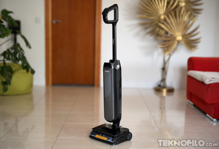 Tineco FLOOR ONE S9 Artist Steam Pro: análisis de sus funciones y opinión Aspiradora vertical negra en salón moderno con suelo de baldosas, sofá rojo, planta y decoración dorada.
