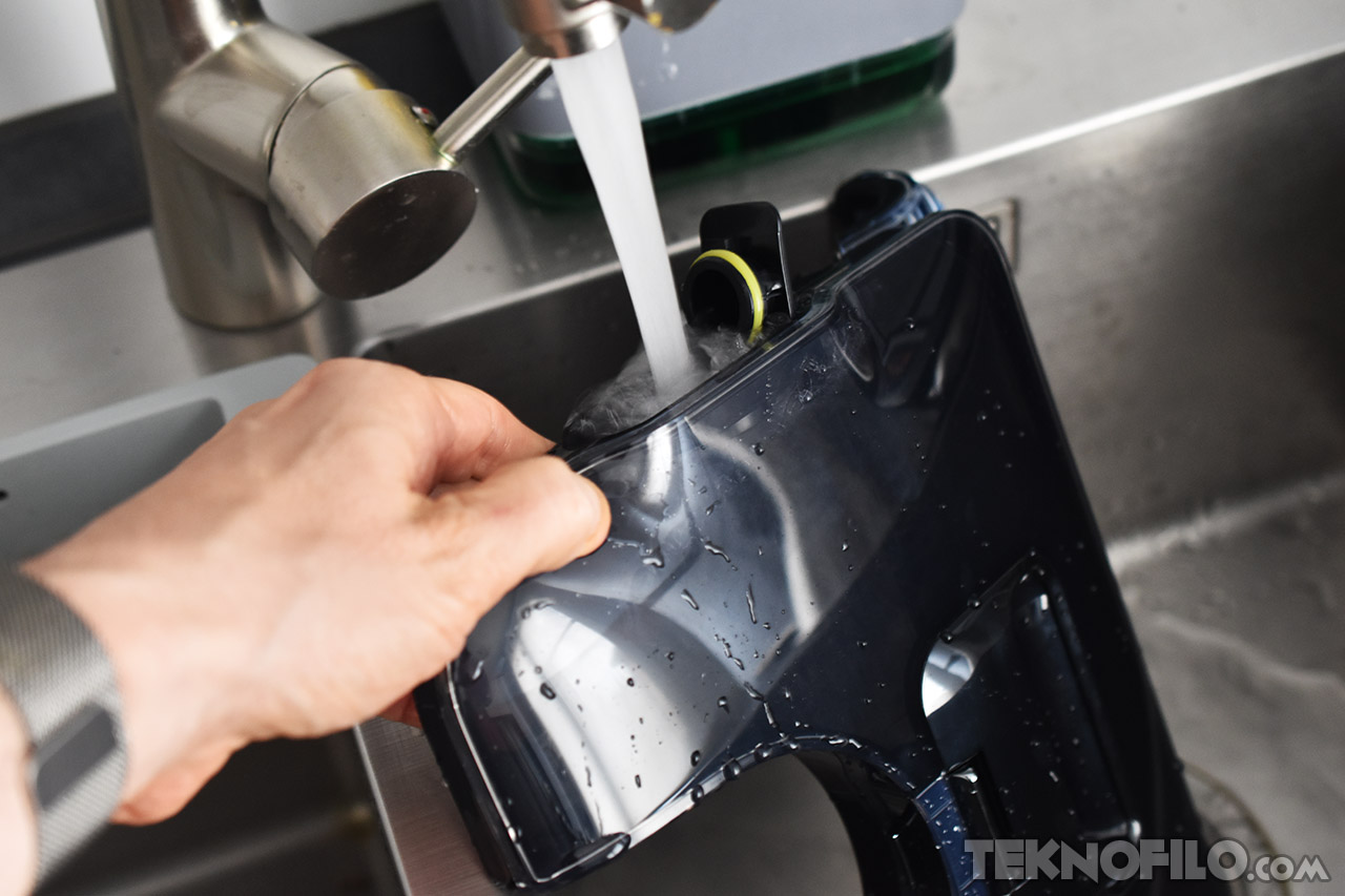 Mano llenando depósito de agua bajo el grifo de una cocina moderna.