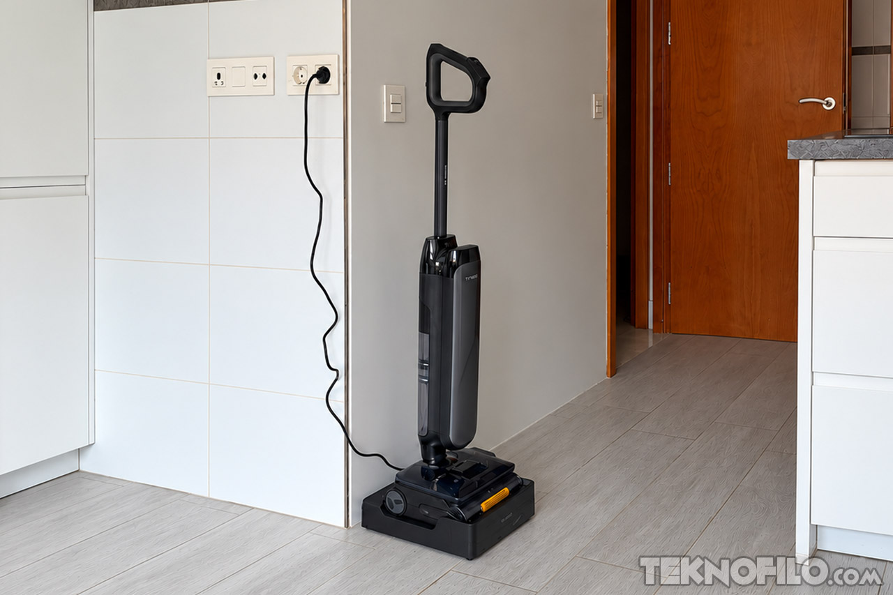 Aspiradora eléctrica negra en base de carga en cocina moderna con piso de cerámica y enchufe en la pared.