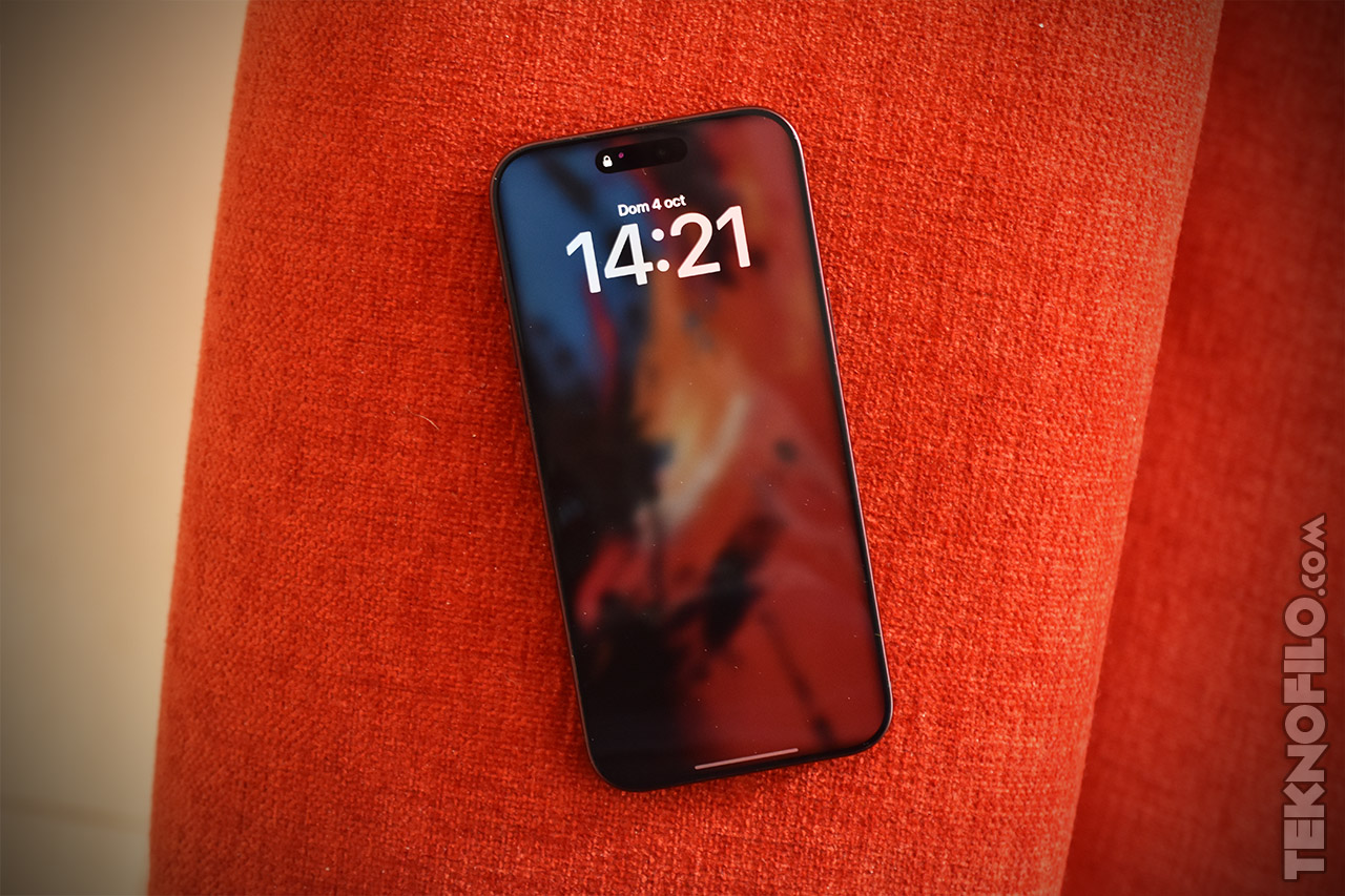 Smartphone moderno sobre sillón naranja, mostrando la hora 14:21 (Dom 4 oct) en la pantalla de bloqueo.