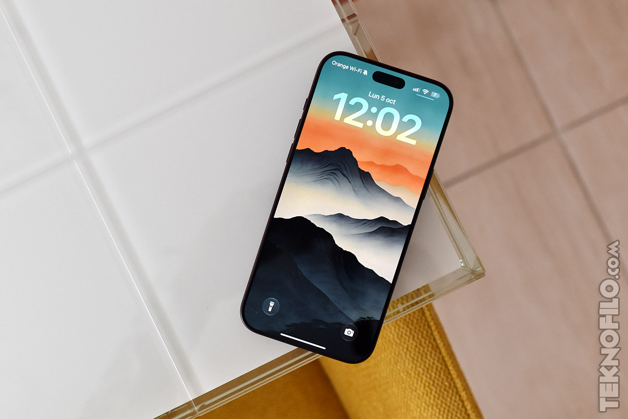 Smartphone sobre mesa blanca con fondo de pantalla de montañas y hora visible, 12:02, diseño moderno y elegante.