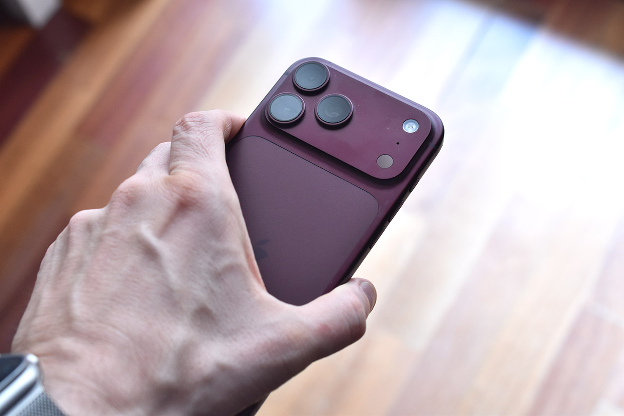 Persona sosteniendo un teléfono móvil de color púrpura con triple cámara en parte trasera sobre suelo de madera.