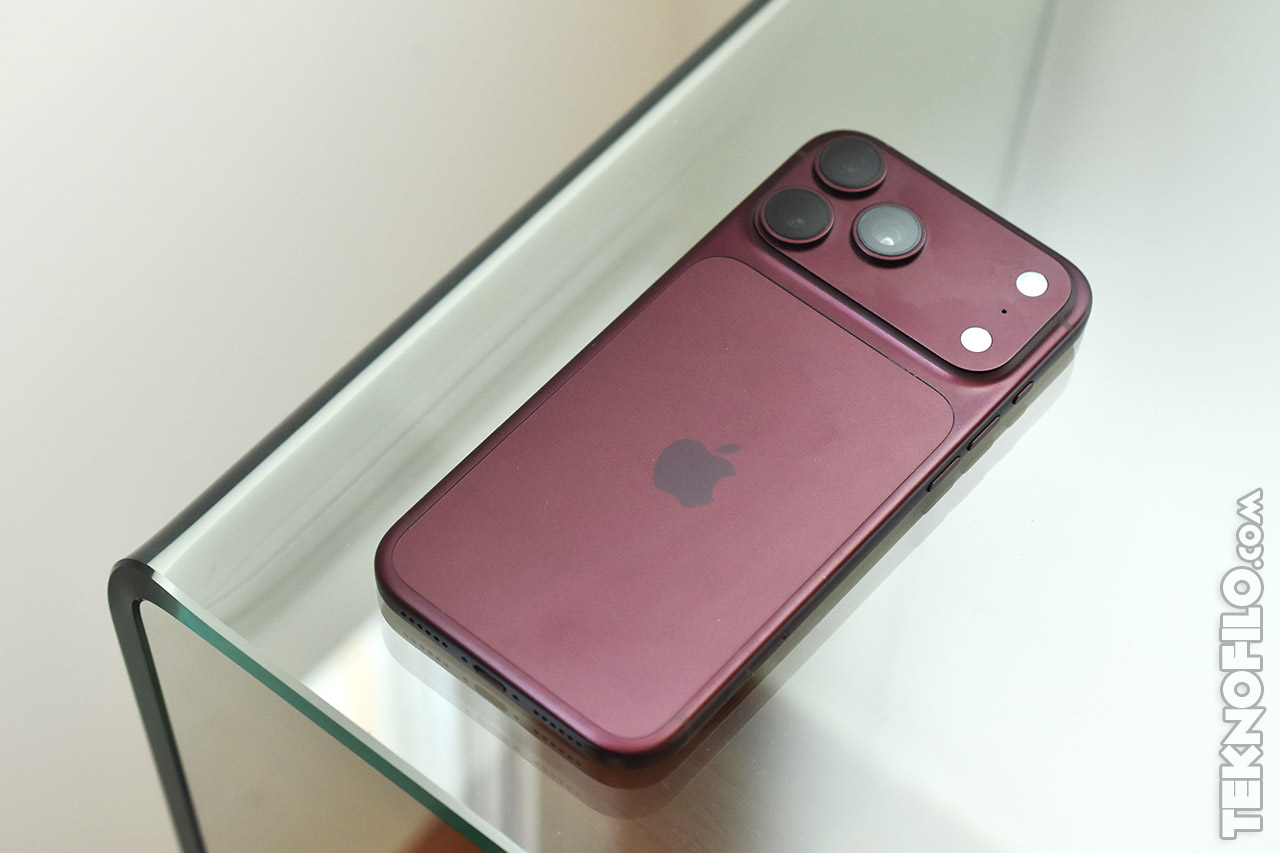 Smartphone iPhone color rojo oscuro sobre mesa de vidrio, mostrando su diseño trasero con triple cámara.