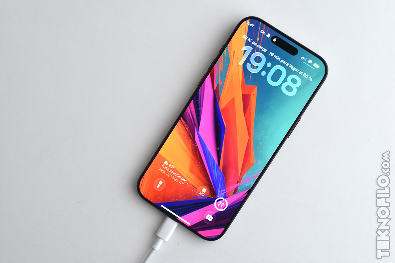 Smartphone con pantalla colorida cargando con cable blanco sobre fondo blanco, mostrando hora y nivel de carga.