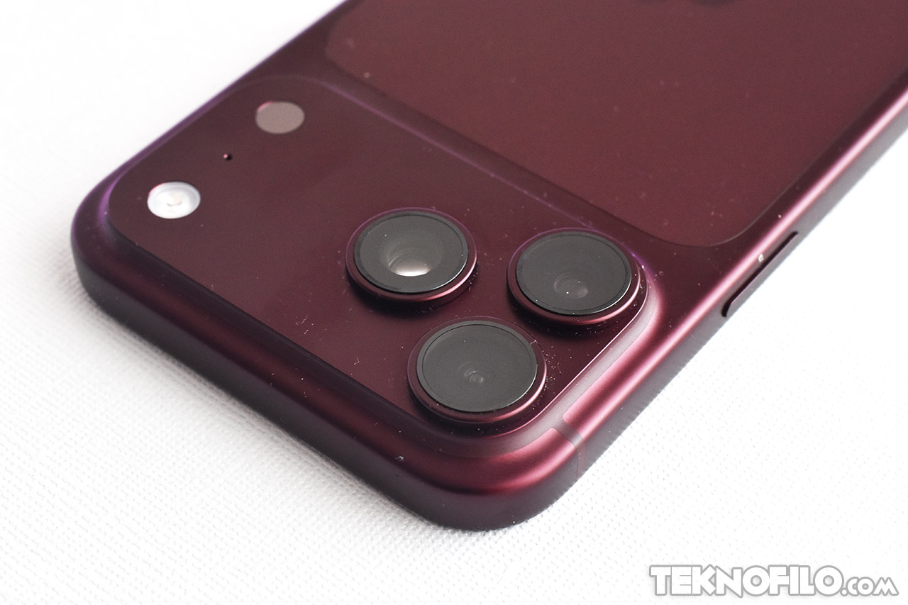 Cámara trasera de un smartphone rojo oscuro con triple lente sobre fondo blanco.