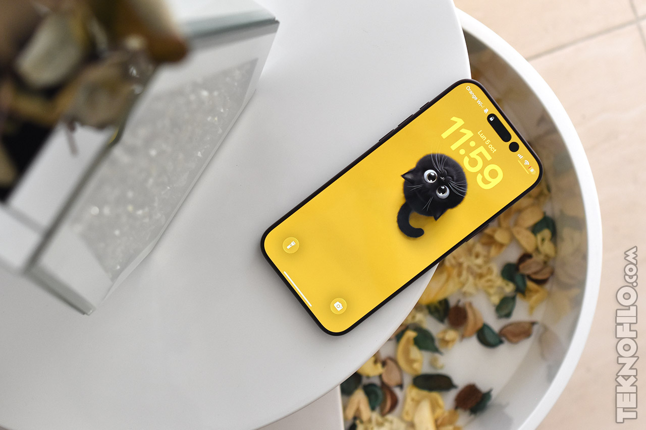 Teléfono inteligente con fondo amarillo de un gatito negro sobre una mesa blanca, rodeado de decoración otoñal.