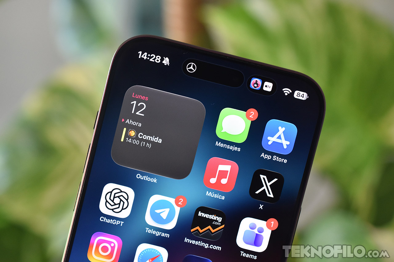 Primer plano de pantalla de iPhone con aplicaciones como Mensajes, App Store y recordatorio de comida a las 14:00.