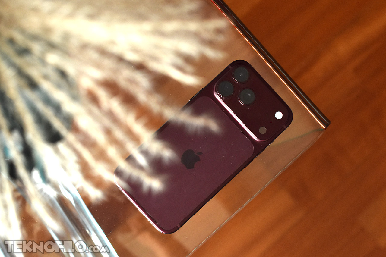 Smartphone con tres cámaras sobre mesa de vidrio, resaltando diseño moderno y elegante en ambiente cálido.