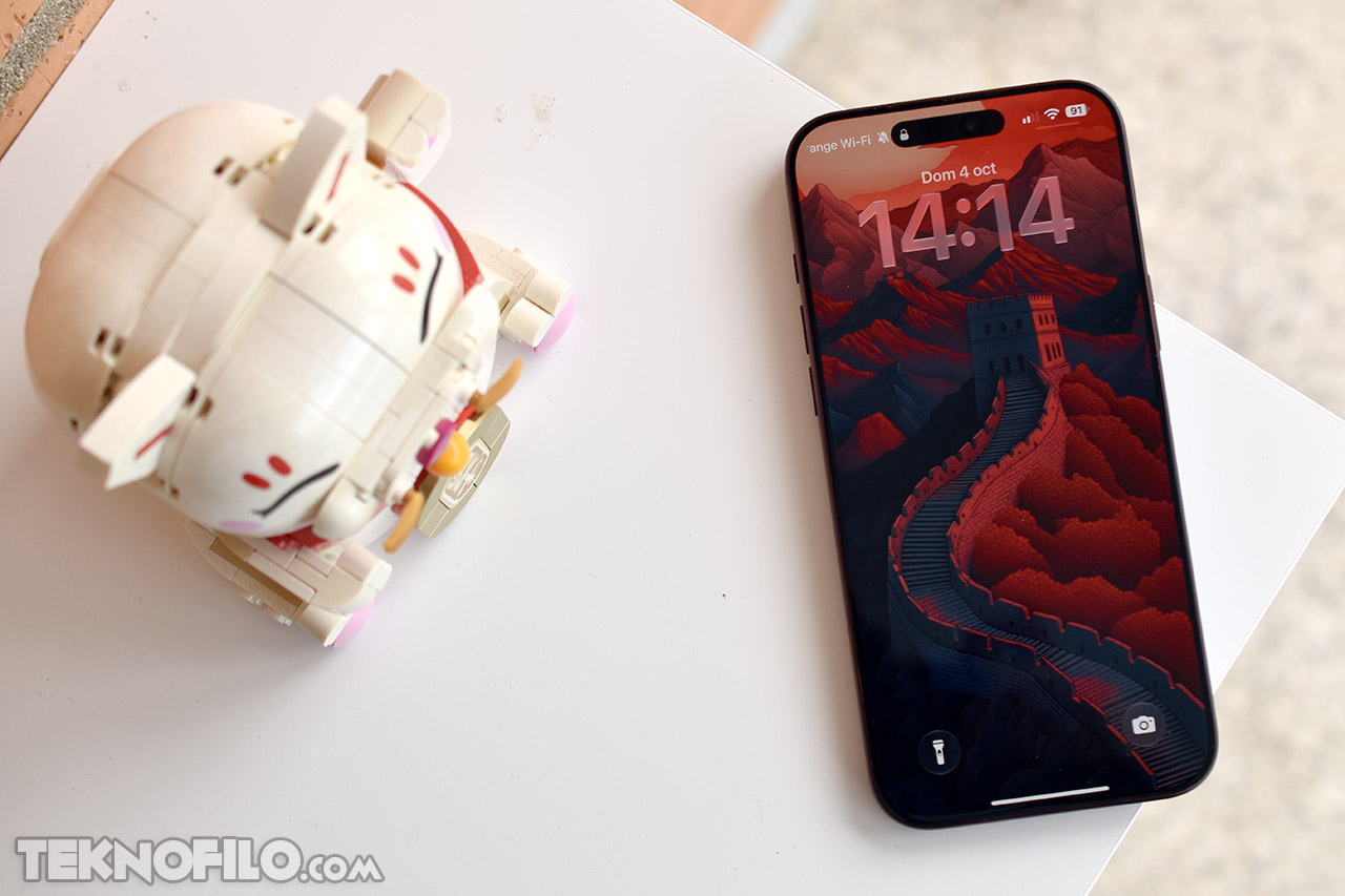 Teléfono inteligente con fondo de pantalla de la Gran Muralla China junto a un juguete robot en una mesa blanca.