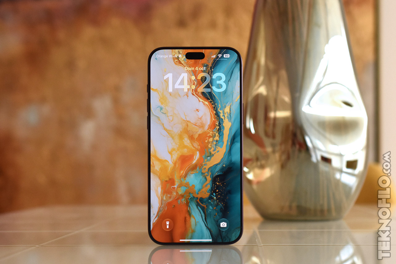 Teléfono móvil con pantalla en colores vibrantes, fondo artístico y elegante decoración de metal detrás.