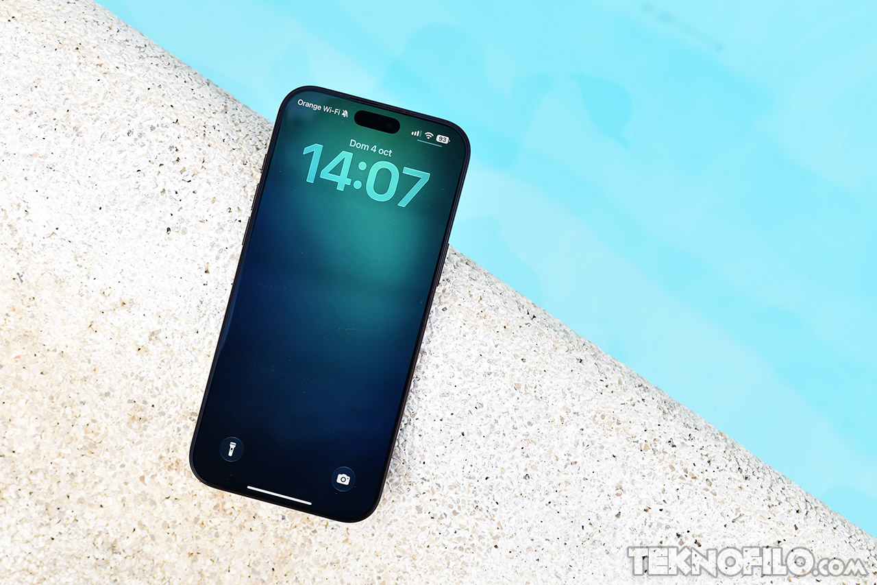 Smartphone moderno junto a una piscina con pantalla encendida mostrando la hora 14:07 y fecha 4 de octubre.