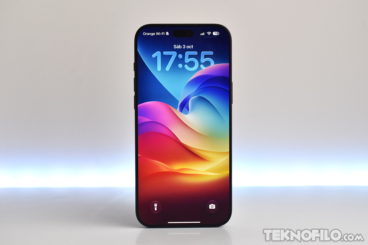 Smartphone con pantalla encendida y fondo multicolor, exhibiendo la hora 17:55 en un ambiente neutro.