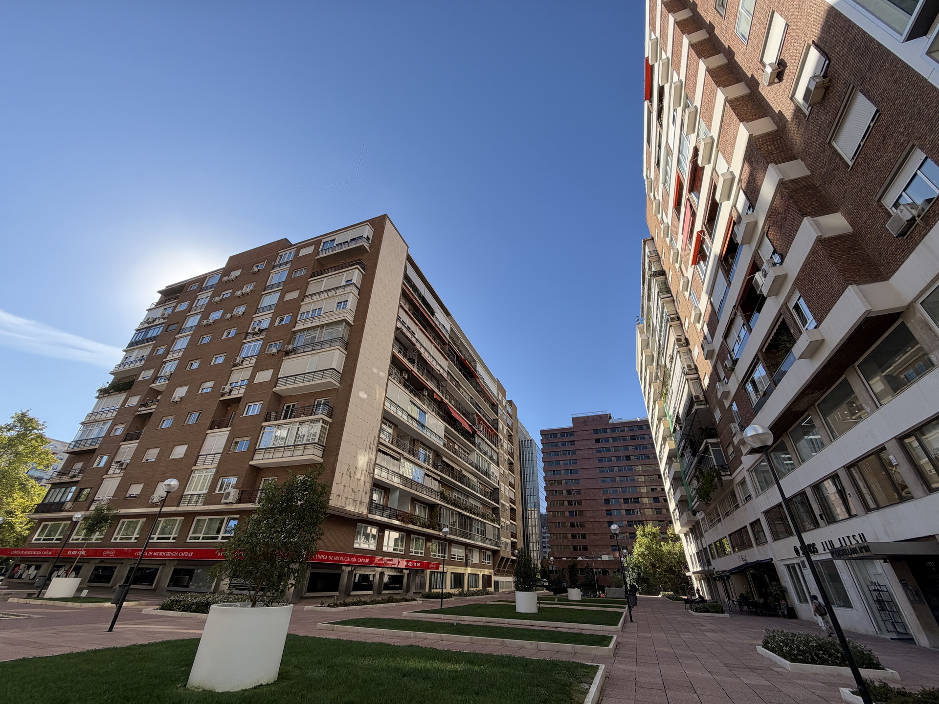 Edificios residenciales de ladrillo rojo bajo un cielo despejado y soleado en una plaza urbana con áreas verdes.
