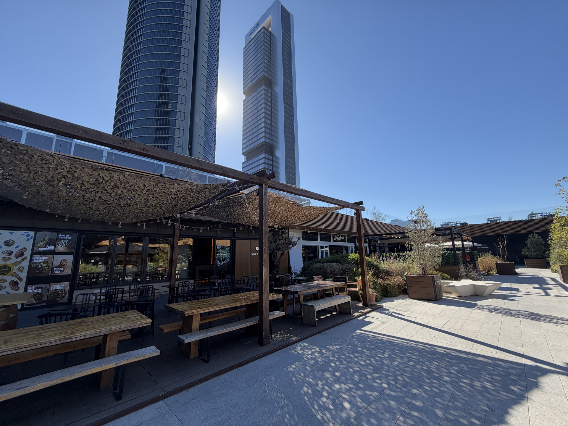 Terraza al aire libre de un restaurante con rascacielos al fondo en un día soleado.
