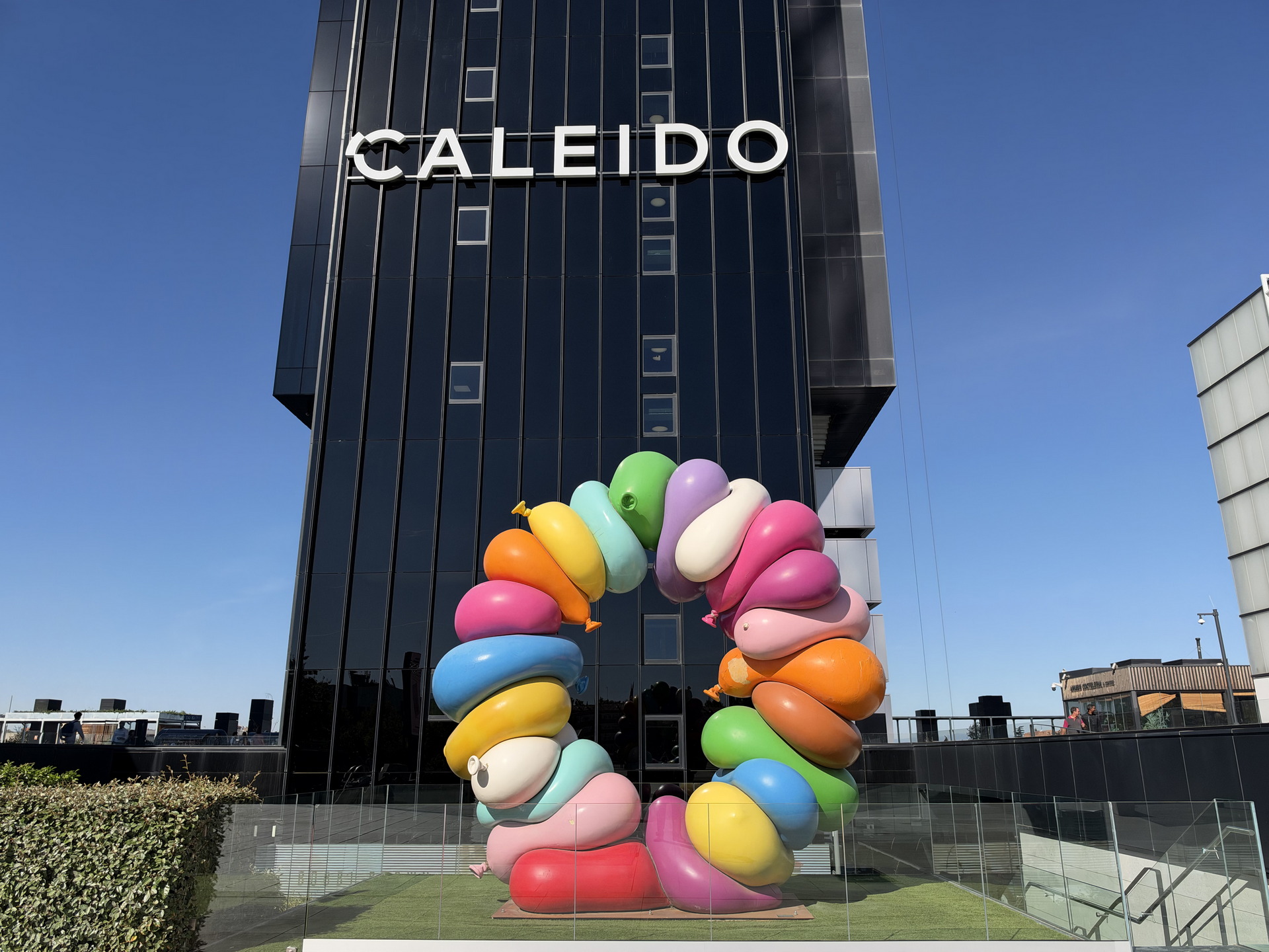 Escultura colorida de formas curvas frente al edificio negro Caleido en un día soleado.
