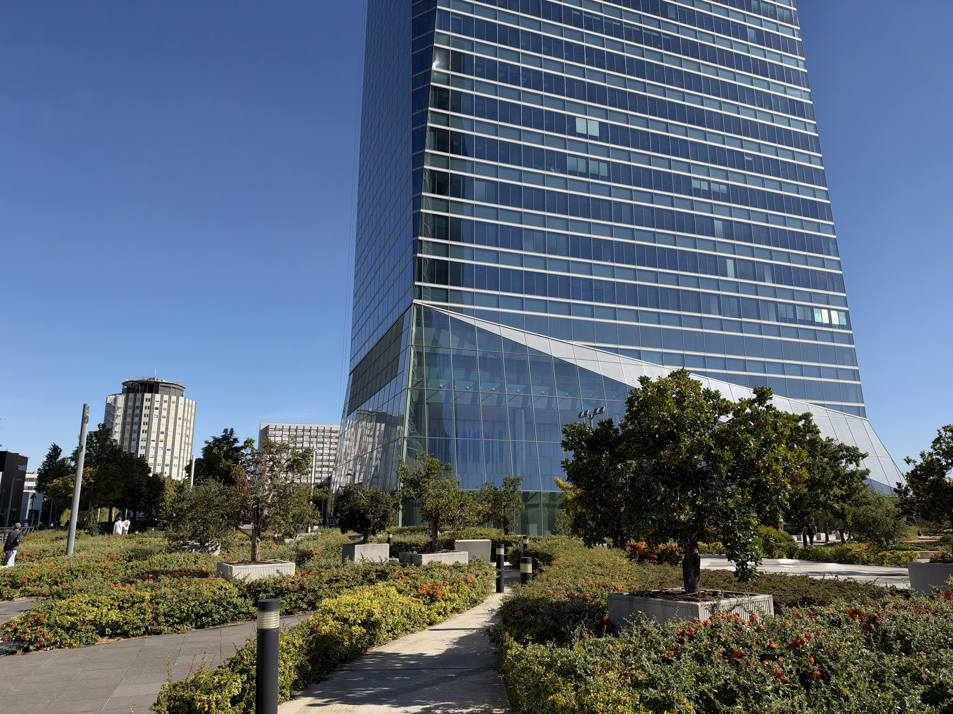 Edificio moderno de cristal con jardines y cielo despejado, destacando arquitectura urbana en día soleado.