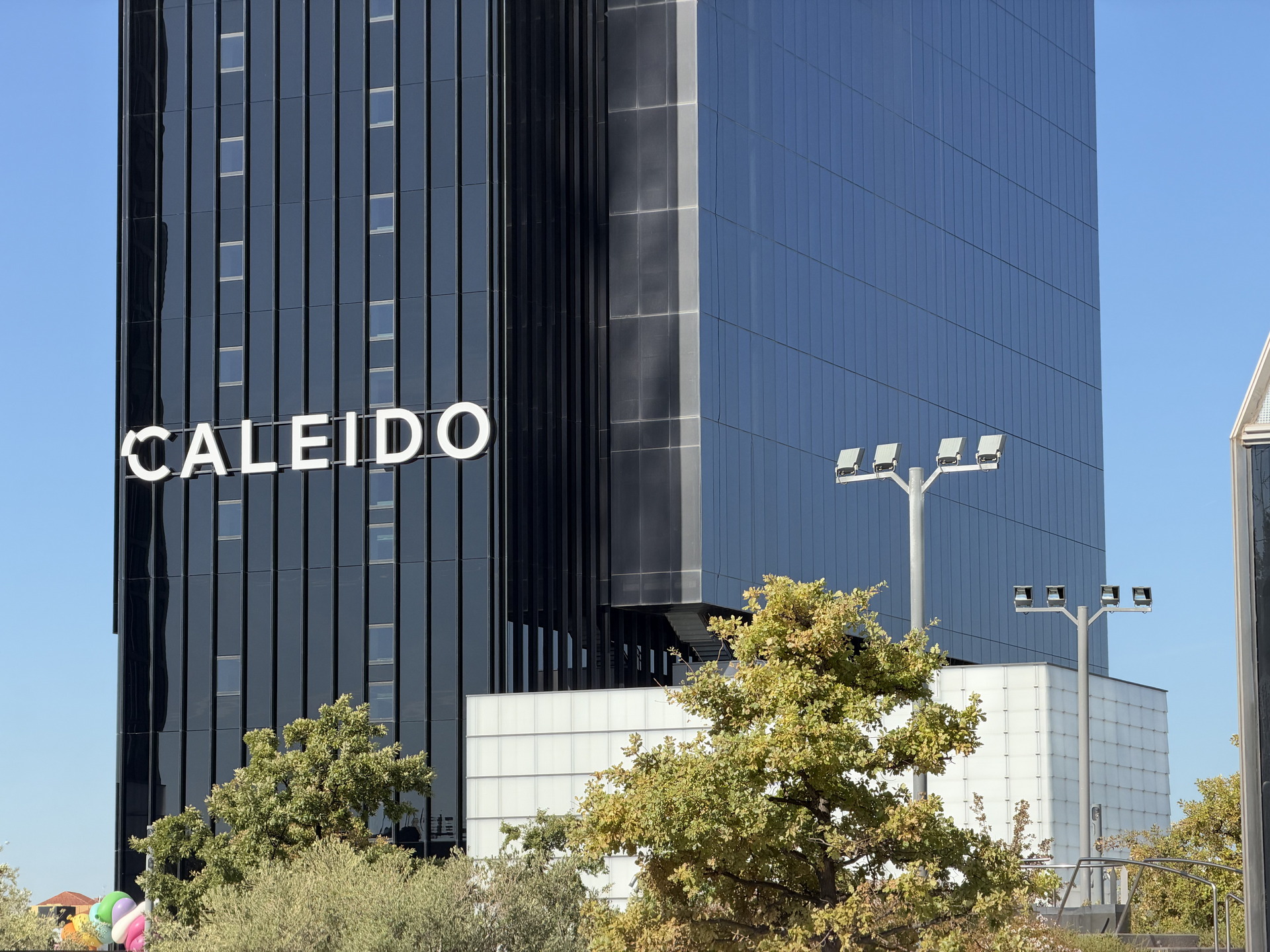 Edificio Caleido en Madrid, arquitectura moderna con fachada de vidrio y árboles en primer plano.