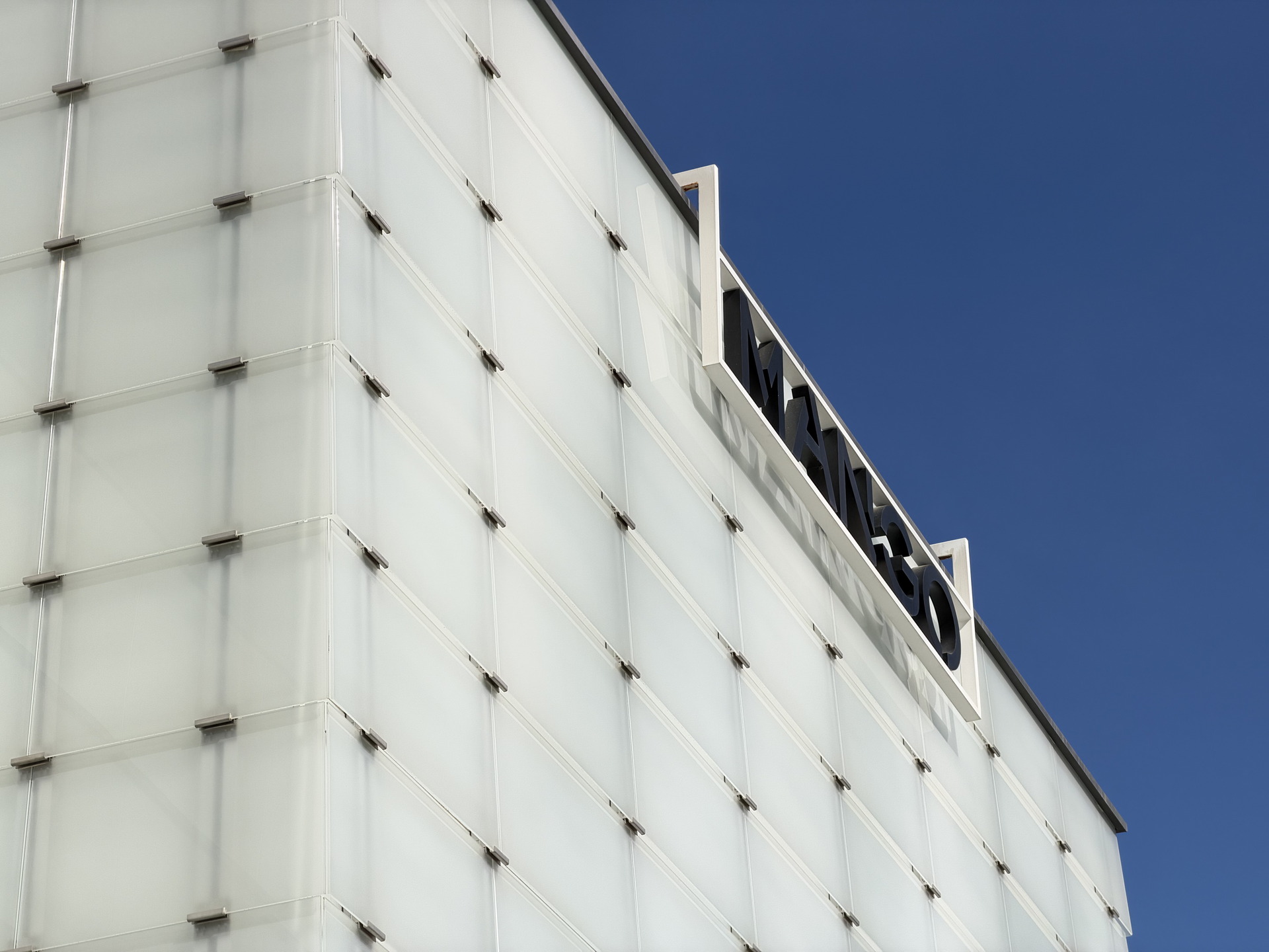 Fachada moderna de edificio con logotipo sobresaliente sobre el cielo azul claro. Diseño arquitectónico contemporáneo.