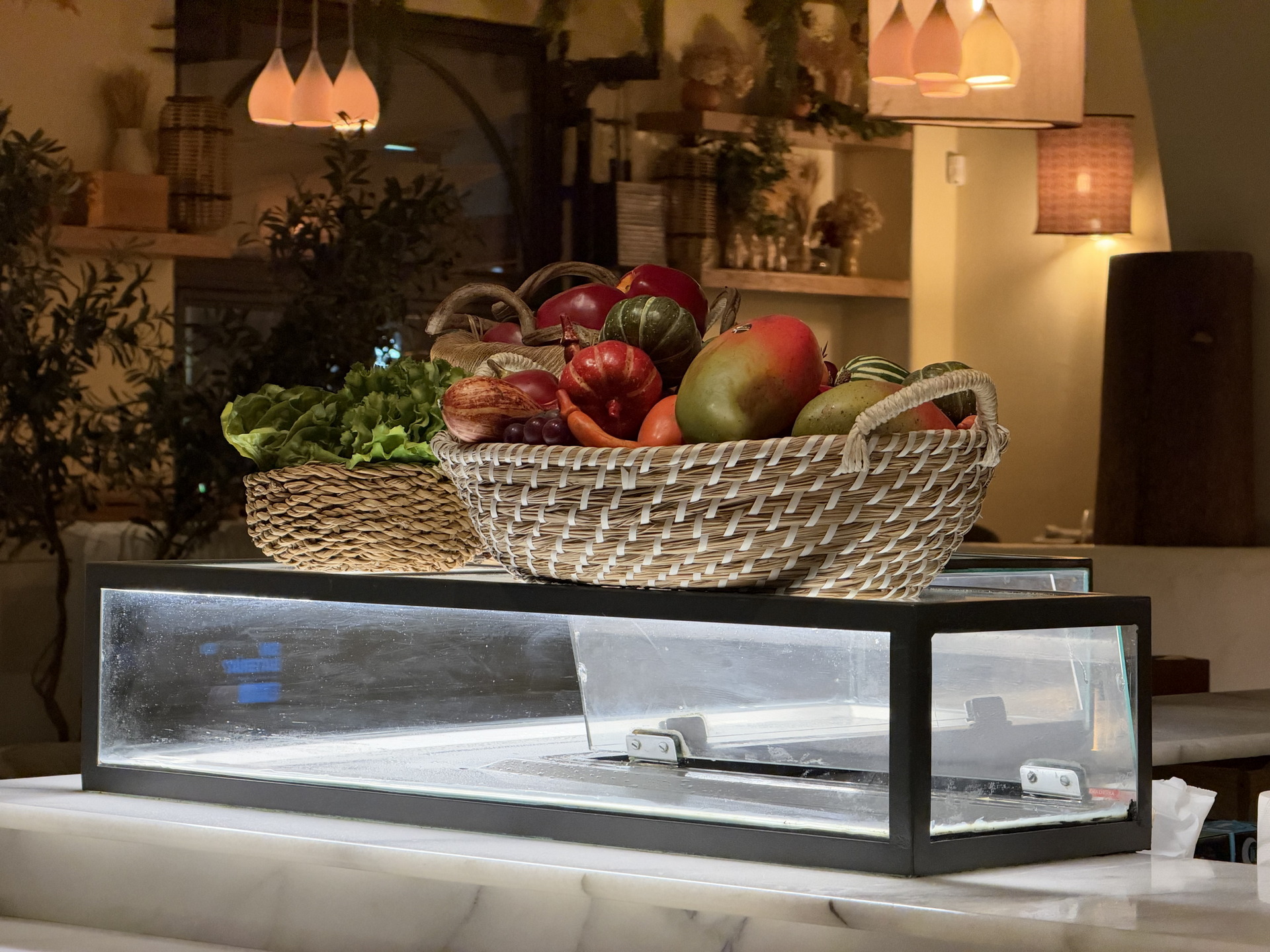 Cestas de mimbre con frutas y verduras frescas sobre mostrador en elegante restaurante iluminado ambientalmente.