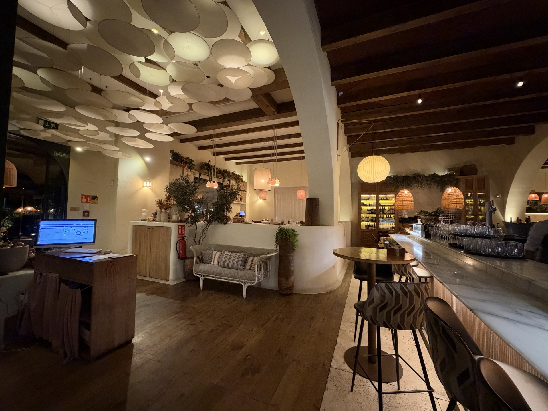Restaurante elegante con iluminación cálida, decoración de madera y barra de mármol en ambiente acogedor.