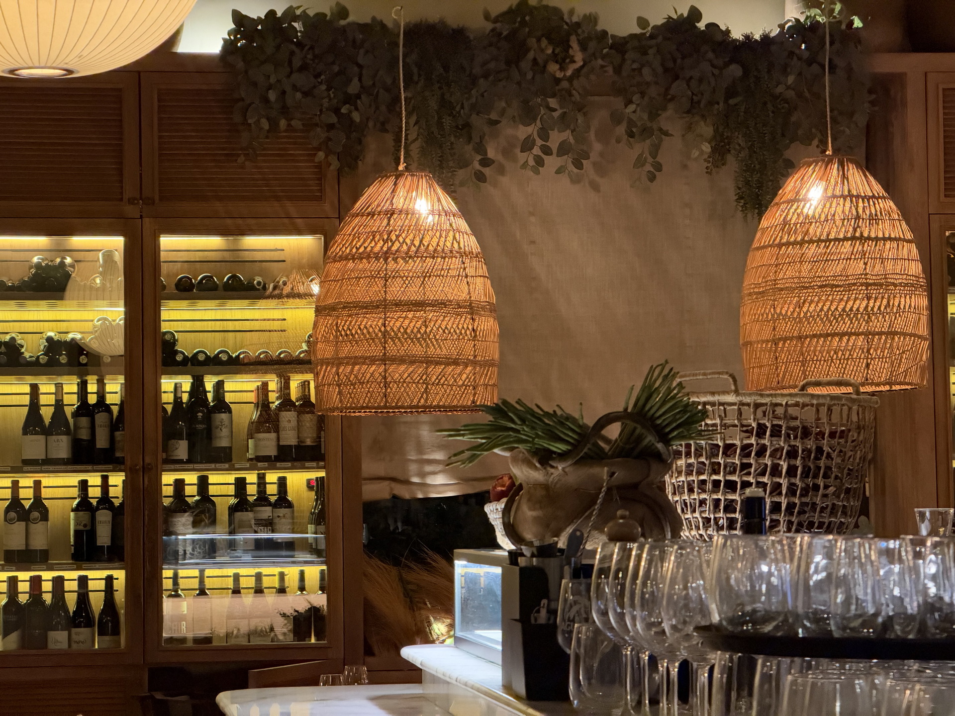 Estante de vinos en un restaurante elegante, iluminado con lámparas tejidas y decoración cálida.