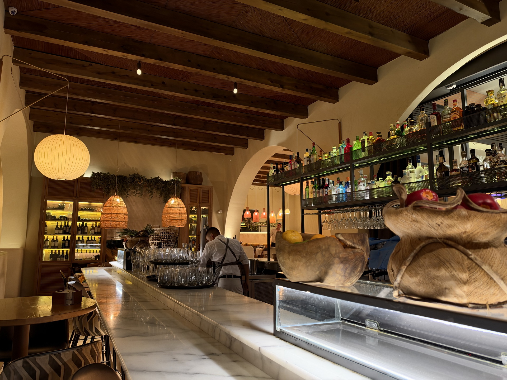Bar acogedor con luces cálidas, estantes de botellas y decoración rústica. Camarero preparando bebidas.