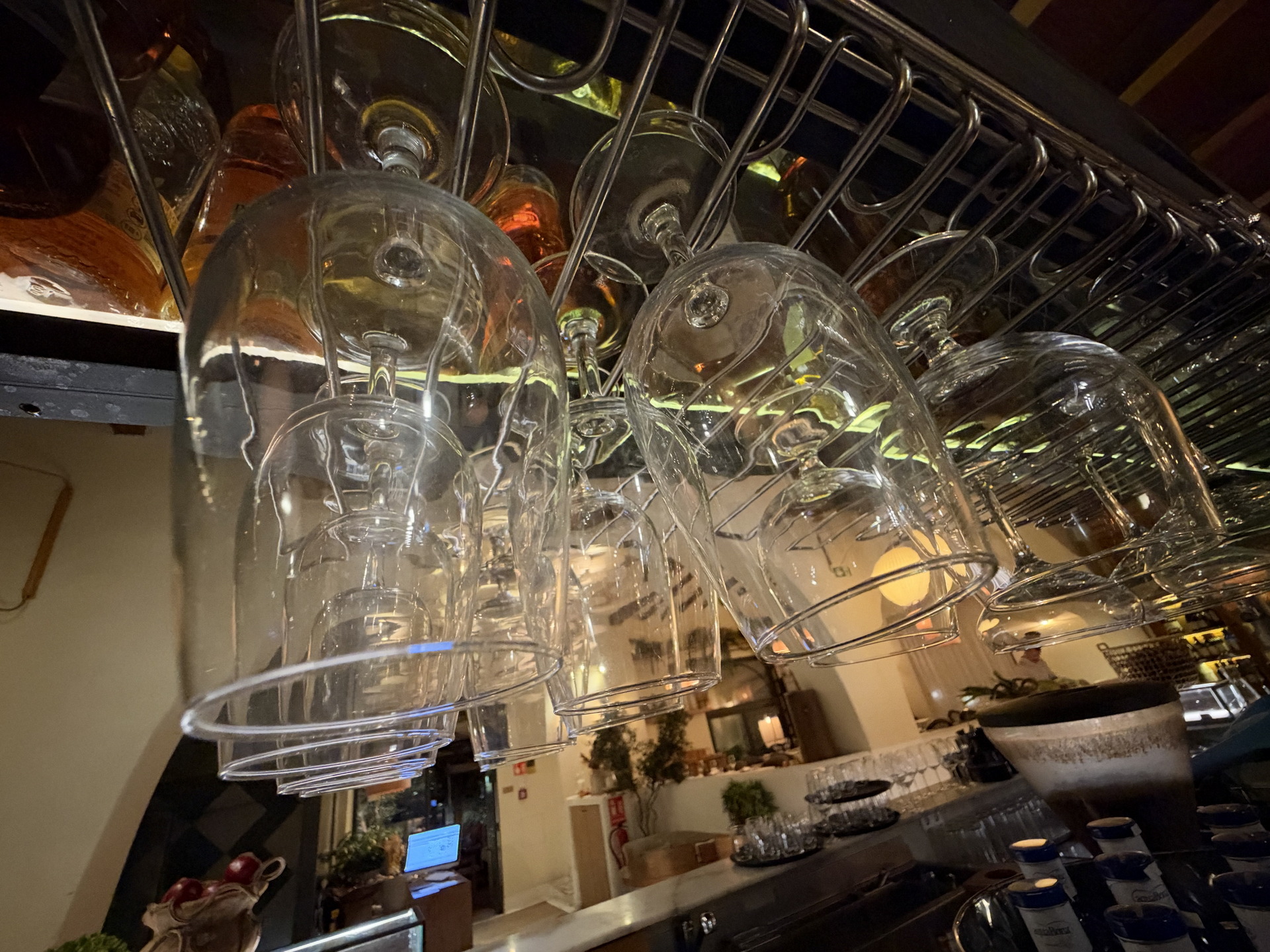 Copas de cristal colgadas boca abajo sobre una barra de bar elegante, con iluminación cálida y ambiente acogedor.