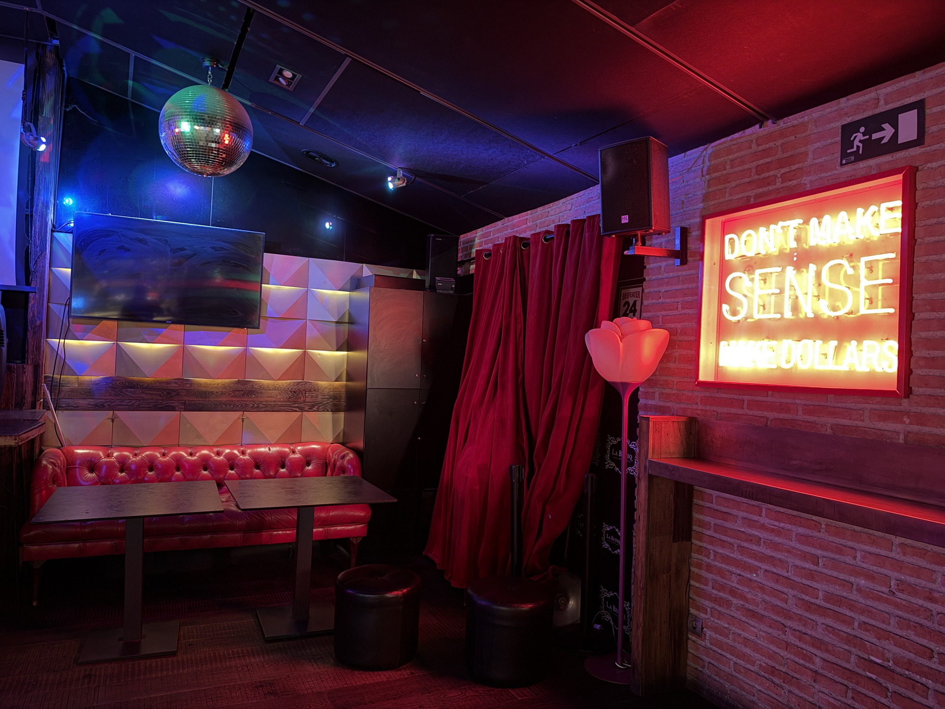 Sala de bar con sofá rojo, bola de discoteca y letrero de neón que dice DON'T MAKE SENSE MAKE DOLLARS.