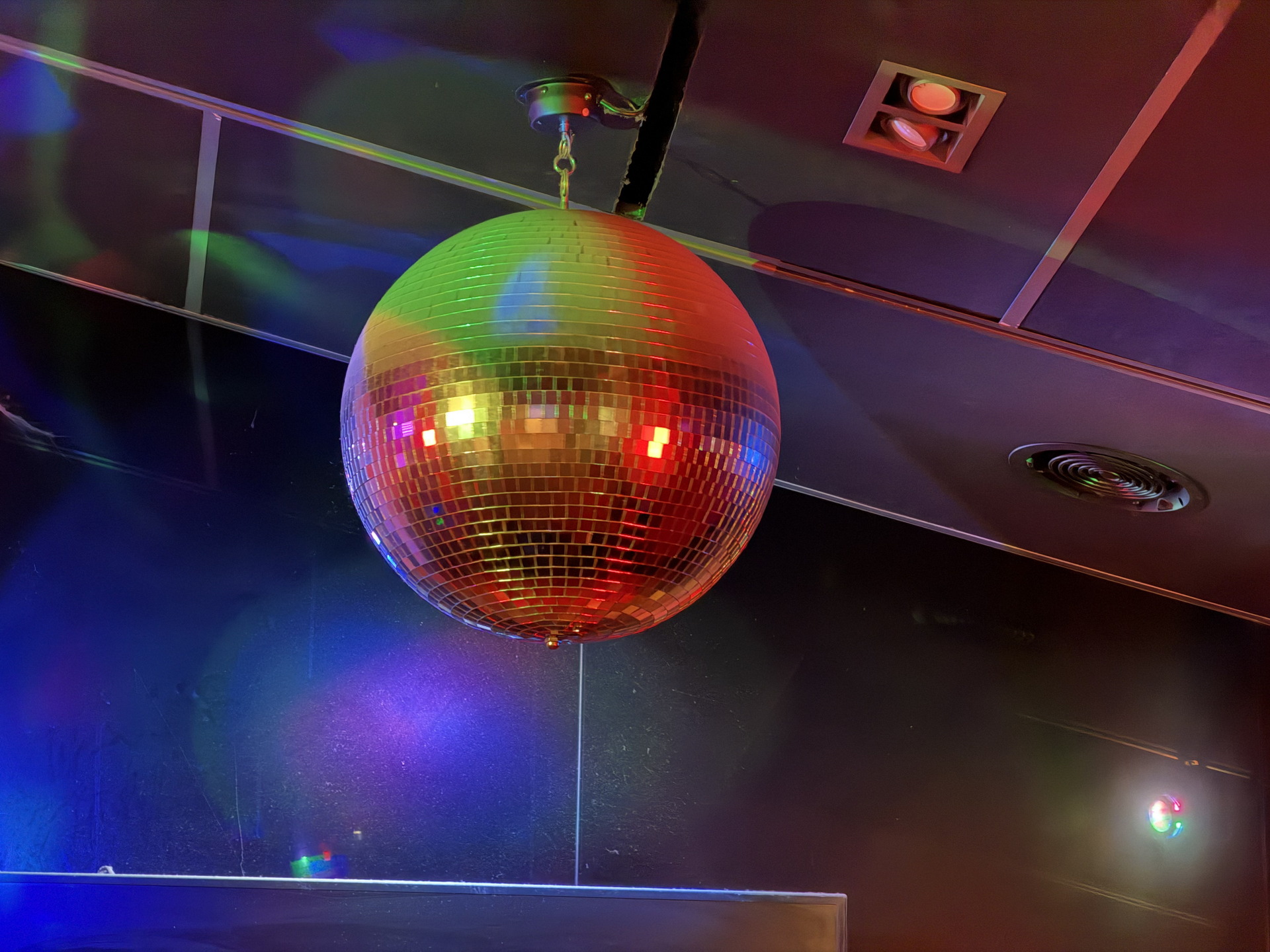 Bola de discoteca colgada en el techo, reflejando luces de colores en una sala oscura de fiesta.