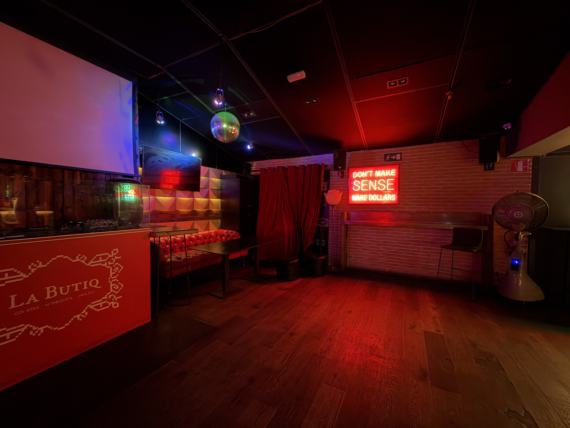 Interior de un bar con luces de neón rojas y decoración moderna, con pista de baile y mesa junto a la pared.