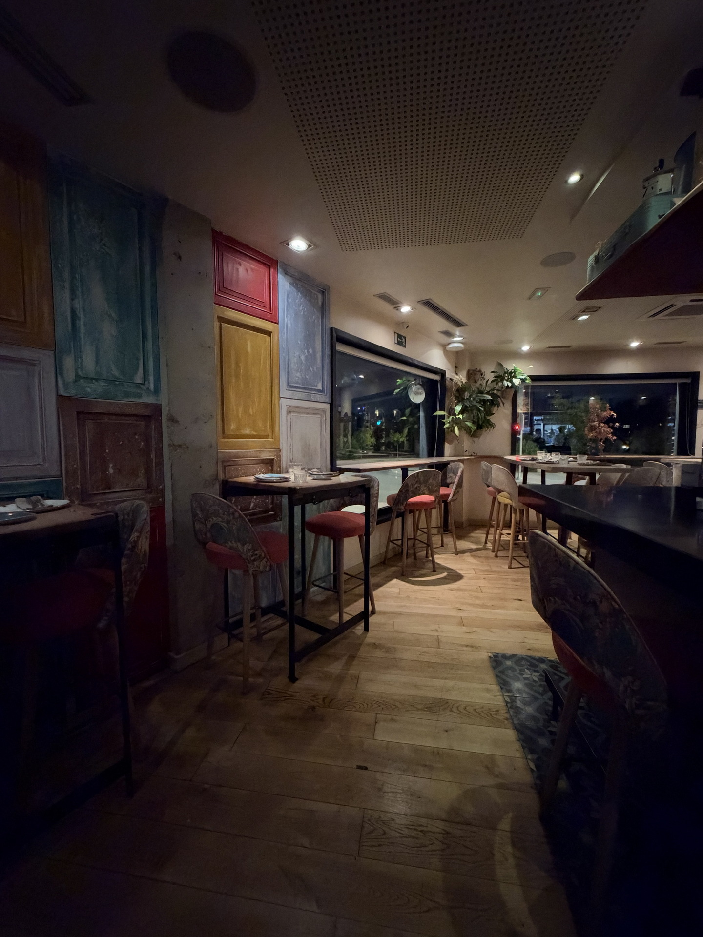 Restaurante acogedor con sillas coloridas y decoración de puertas en la pared, iluminación cálida, ambiente nocturno.