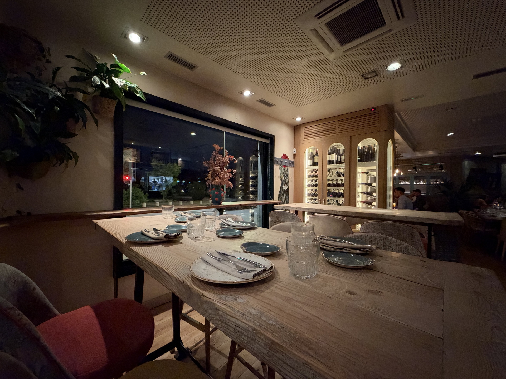 Mesa de restaurante elegante con platos y vasos, ambiente acogedor de noche, estantería de vinos al fondo.