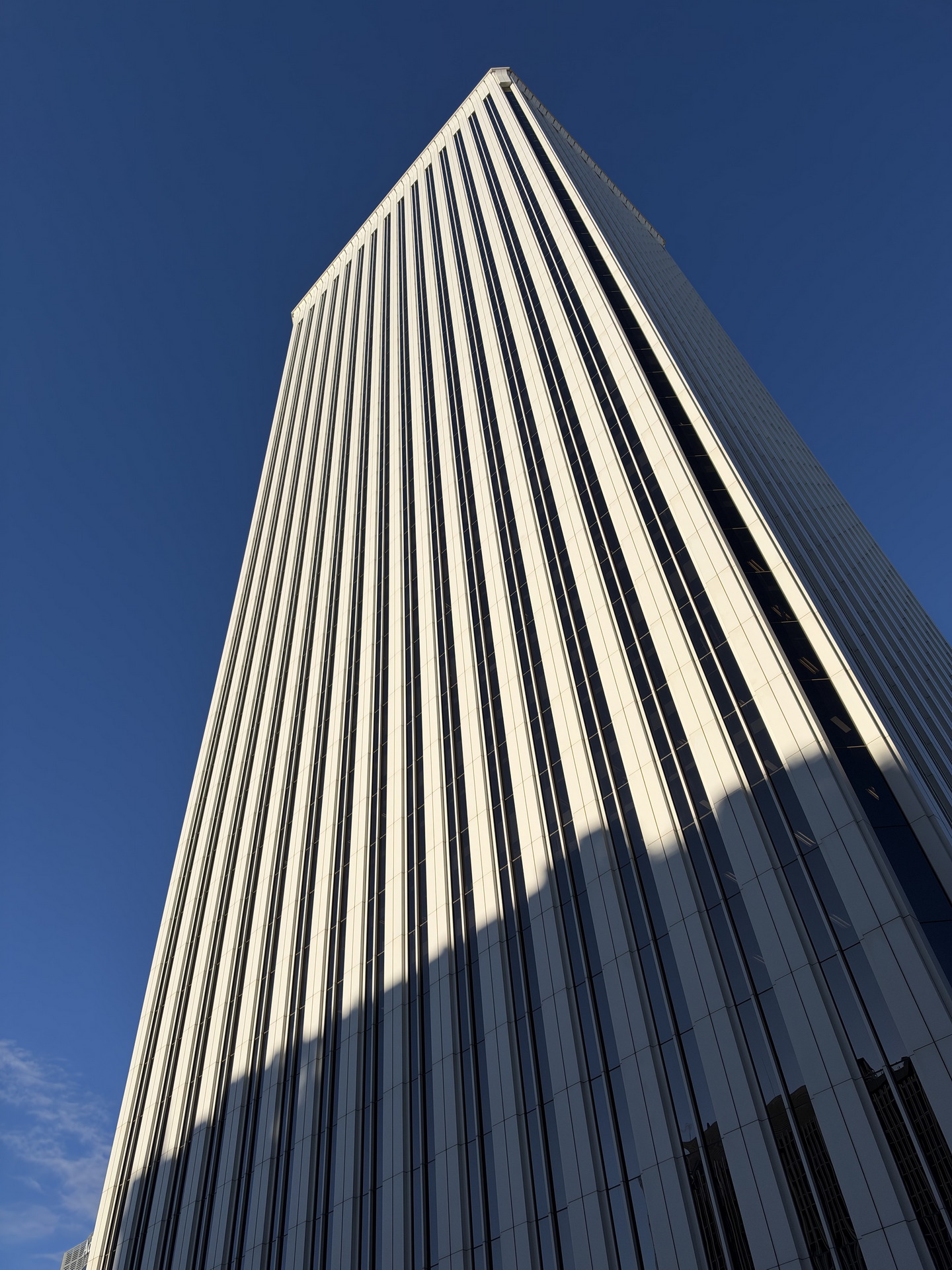 Rascacielos moderno en ángulo ascendente, cielo azul despejado, líneas verticales definidas en la fachada.