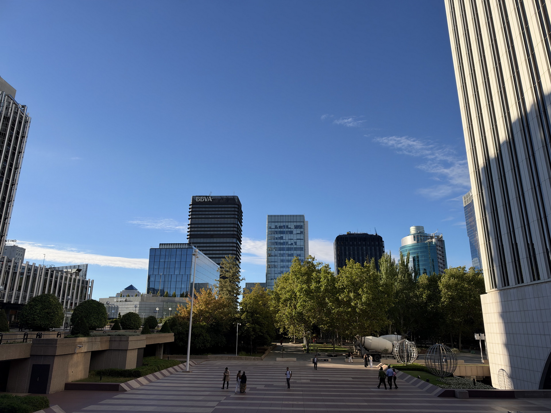 Vista urbana de Madrid, con rascacielos modernos y cielo azul. Personas caminando por el parque en la zona centro.