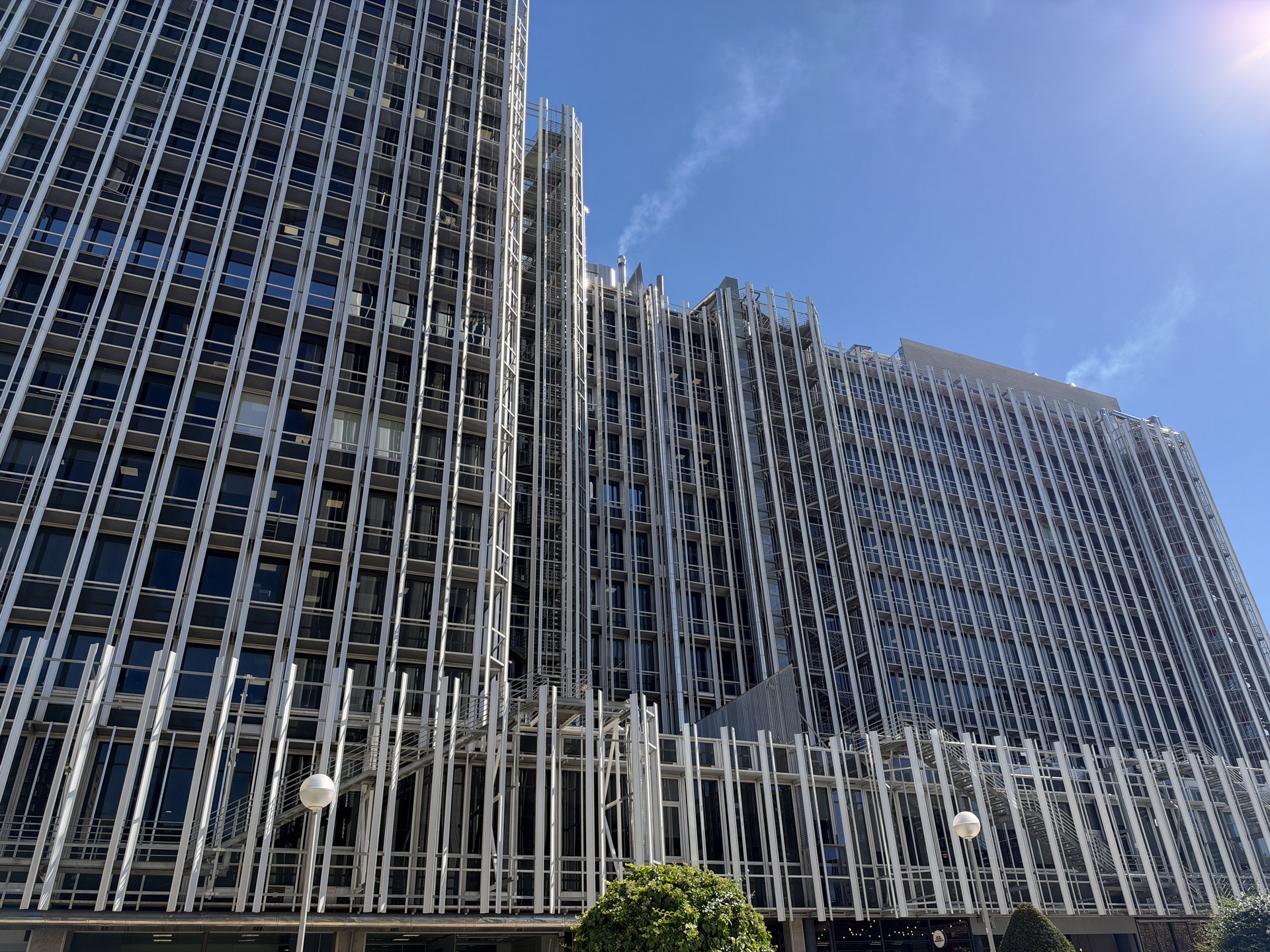 Edificio moderno con fachada de cristal y estructuras metálicas bajo un cielo azul luminoso.