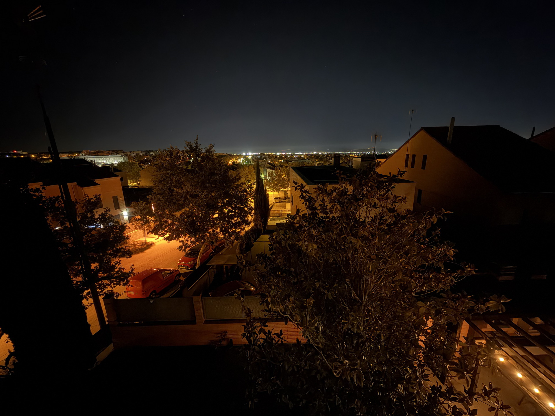 Vista nocturna de un barrio urbano con luces que iluminan calles y casas, destacando el cielo oscuro en el horizonte.