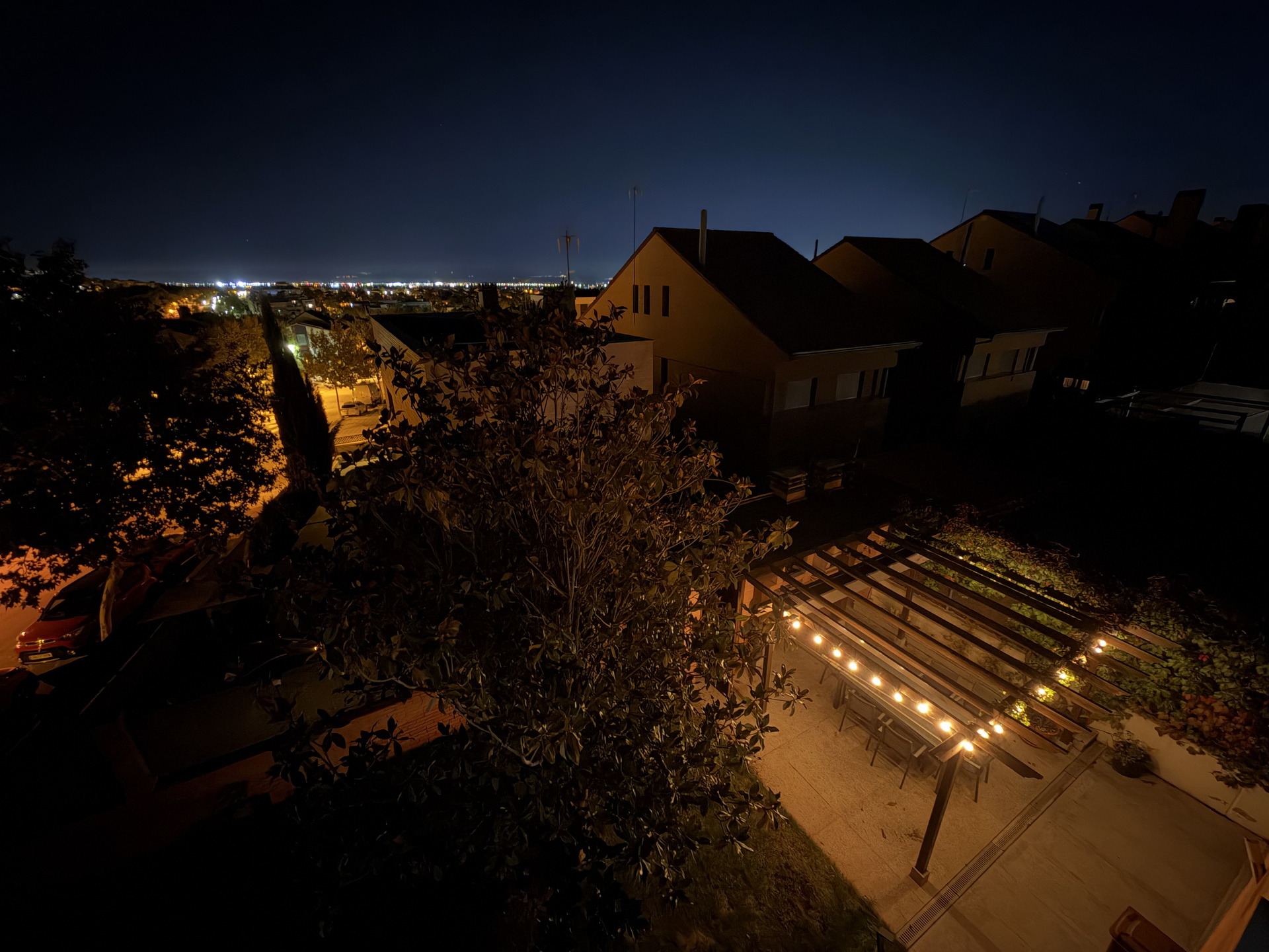 Terraza iluminada en un barrio residencial durante la noche, con vista panorámica de luces de ciudad a lo lejos.