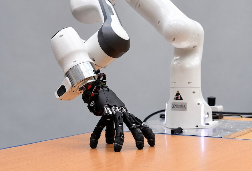 Mano robótica apoyada en una mesa junto a un brazo robótico de laboratorio
